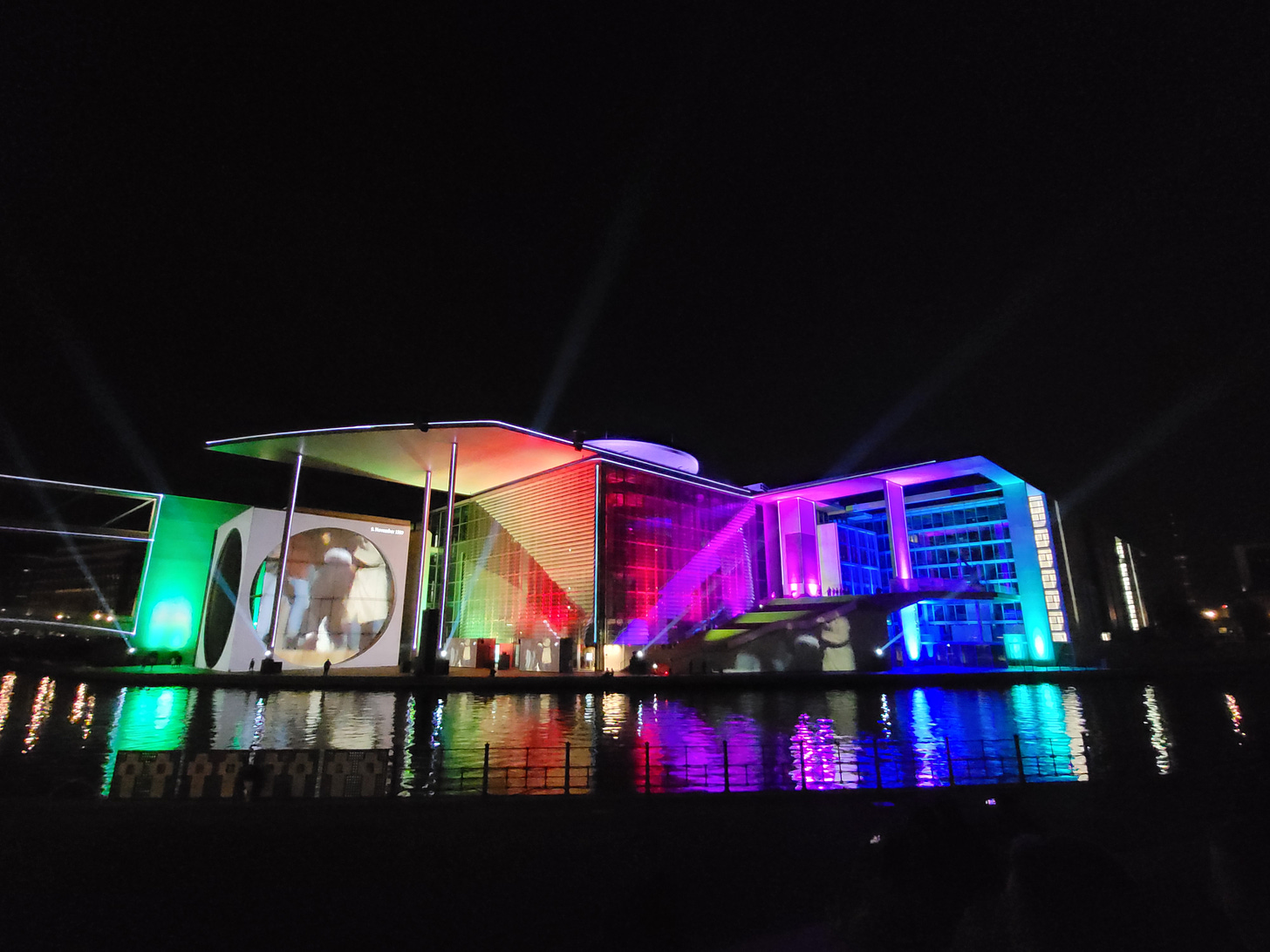 A building lit up in rainbow colours, with a film projected onto part of the wall