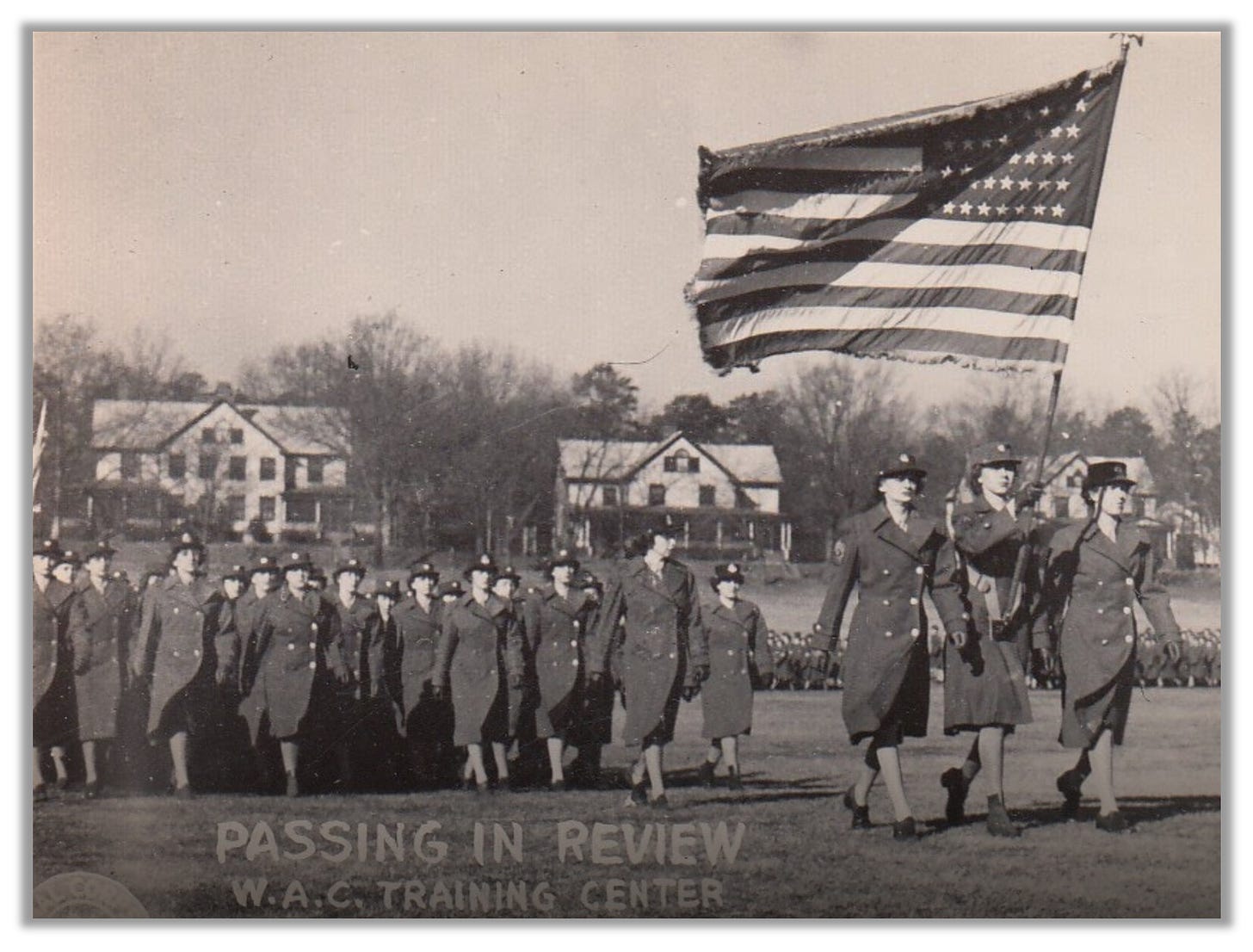 Women in uniform march at a training center in Georgia. A group of three women lead the way, bearing an American flag.