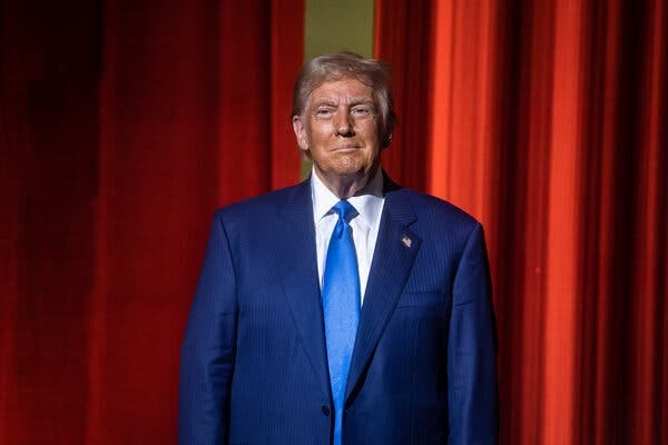 Donald Trump in a blue suit and tie against a red background.