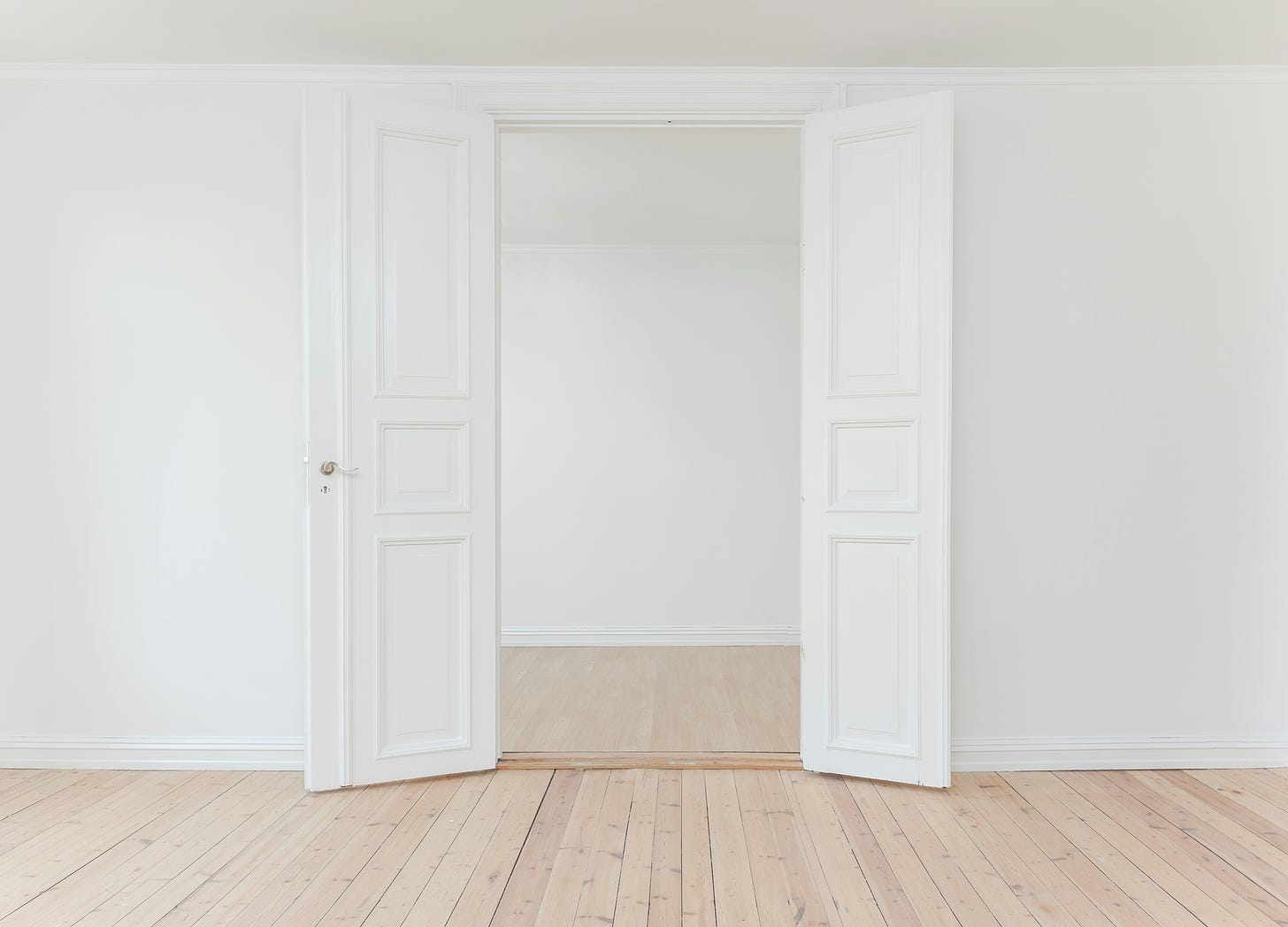 A doorway with two white according doors leading from one space with a wood floor to another. There is a raised bump at the boundary between the two rooms.