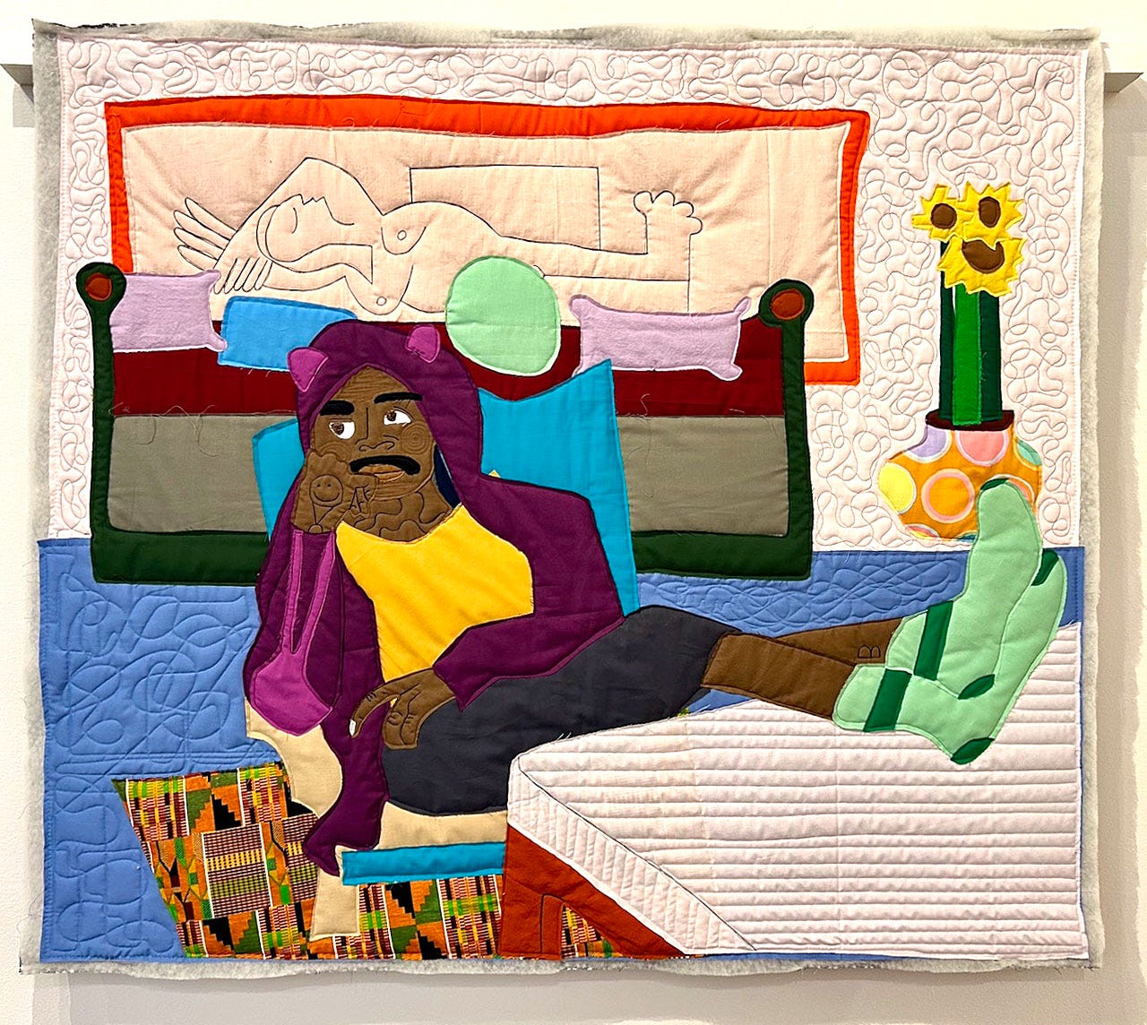 A quilted wall with a person sitting on a bed

Description automatically generated