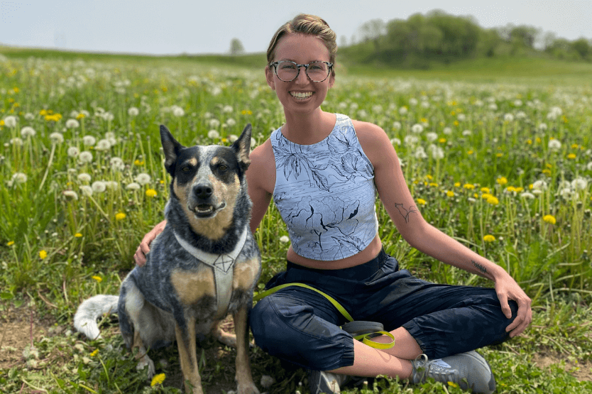 Scout the blue heeler sits in front of a field of wildflowers with her owner, Haley