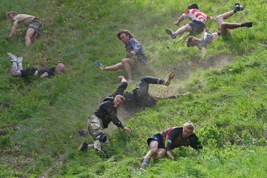 Eight men are seen tumbling and trying to run down a very steep hill.