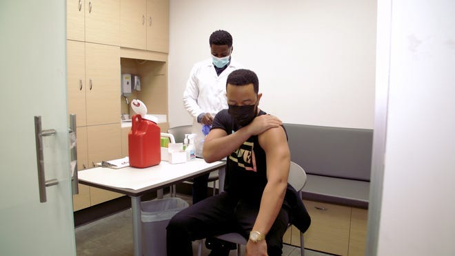 John Legend rolls his sleeve up for the COVD-19 vaccine.