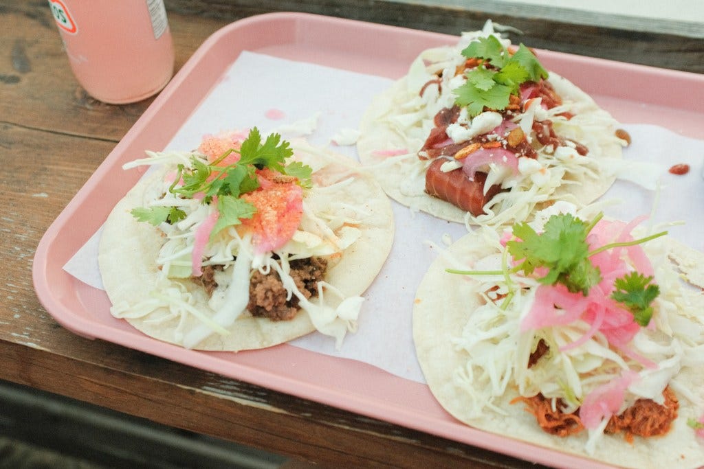 pink tray with three tacos and a pink drink in a glass bottle