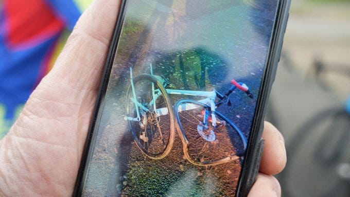 Une homme tient dans sa main un téléphone montrant une photo d'un vélo accidenté