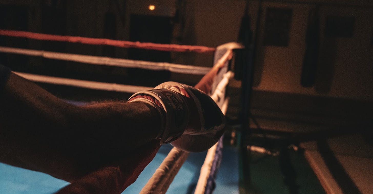 An arm with a boxing glove, resting on the ropes of a boxing ring