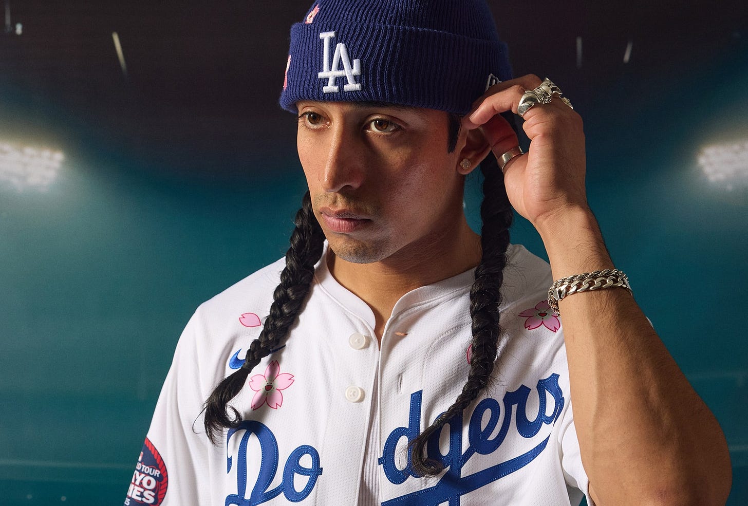 A person wearing a Los Angeles Dodgers jersey with cherry blossom designs, a blue LA beanie, braided hair, and silver jewelry.