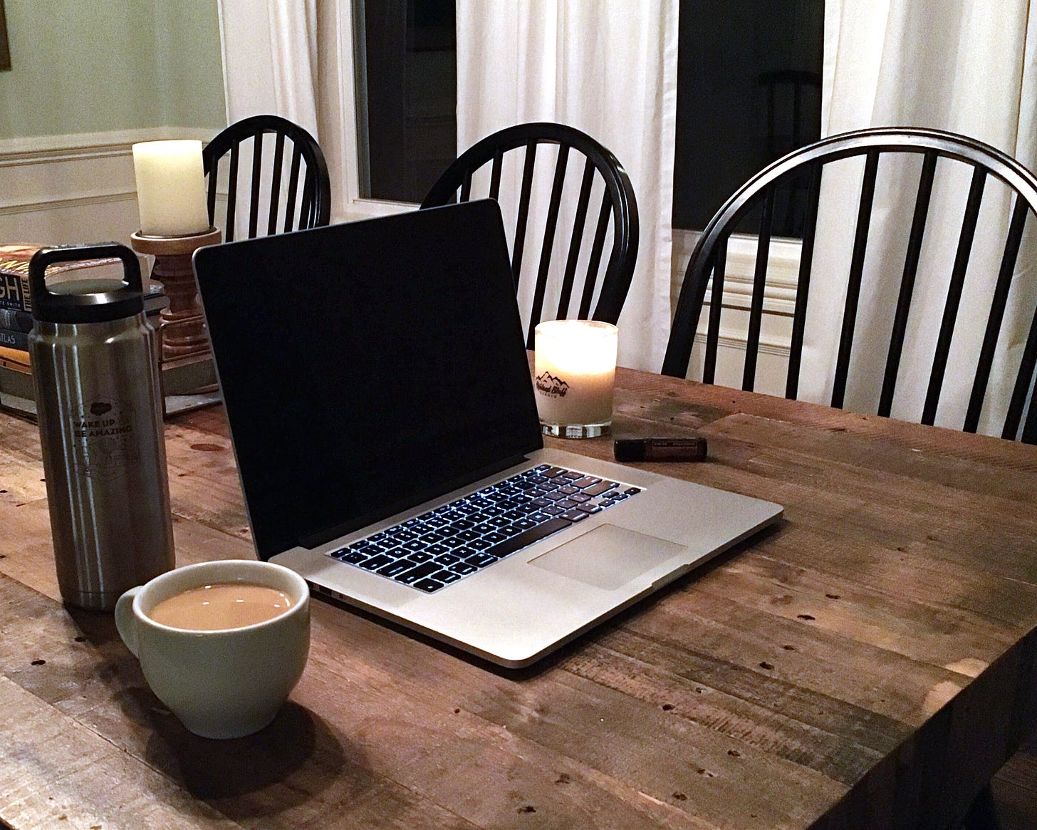 Photo of laptop on table with coffee, candle, and water.