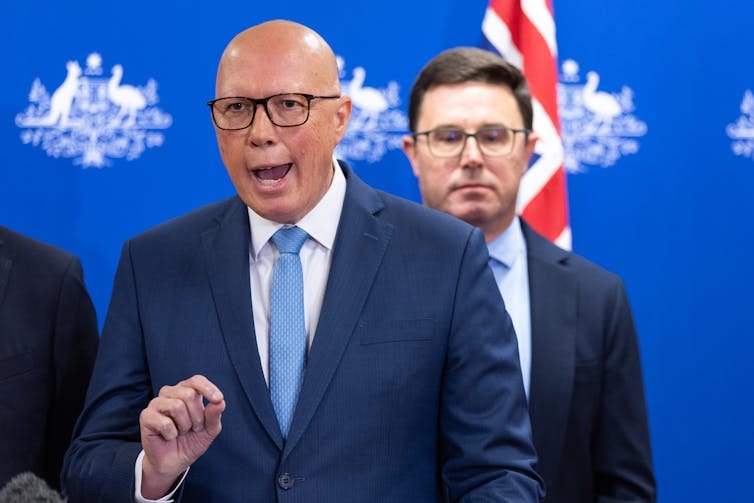 two men stand against blue background