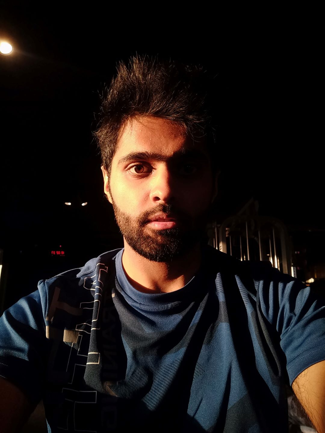 Young Indian man with rough beard staring intensely at the camera lit by harsh shadows