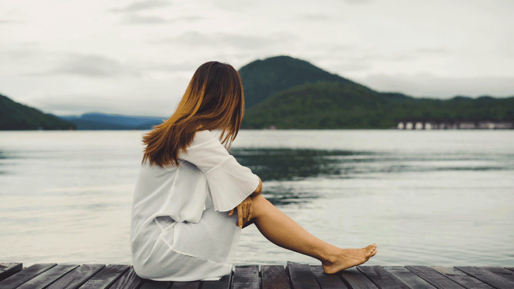 Lonely woman sitting on wooden pier and looking at the lake