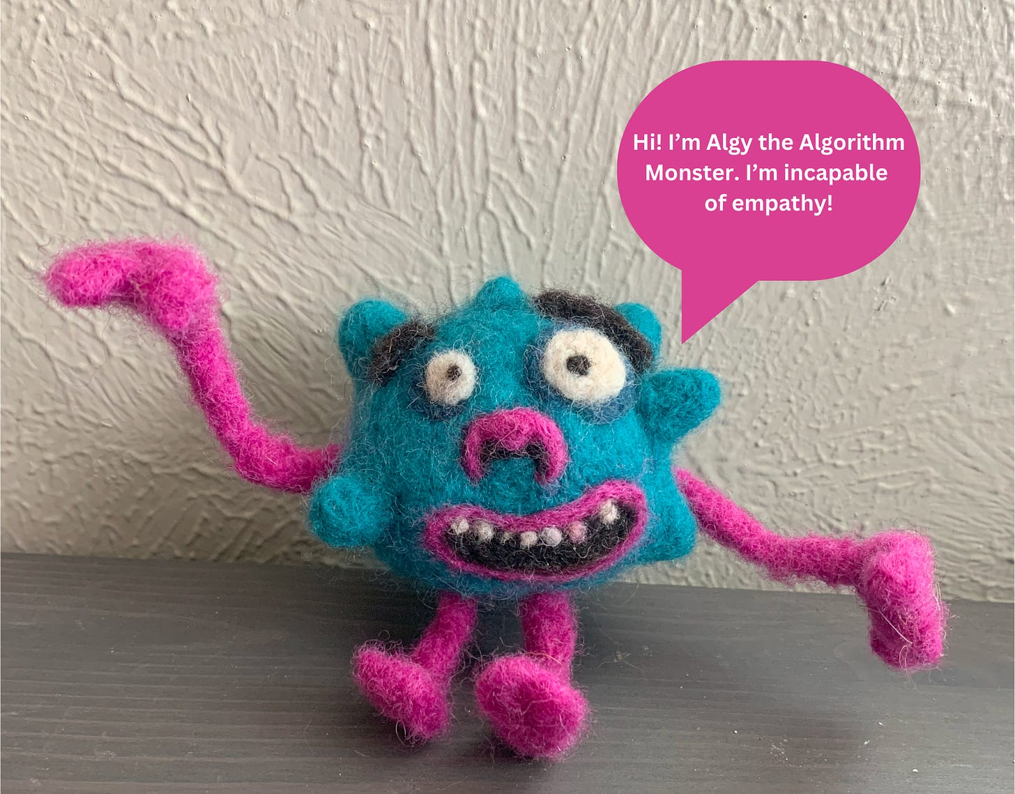 A pink and blue googly eyed monster made of felt with a speech bubble that reads: "Hi! I'm Algy the Algorithm Monster. I'm incapable of empathy!"
