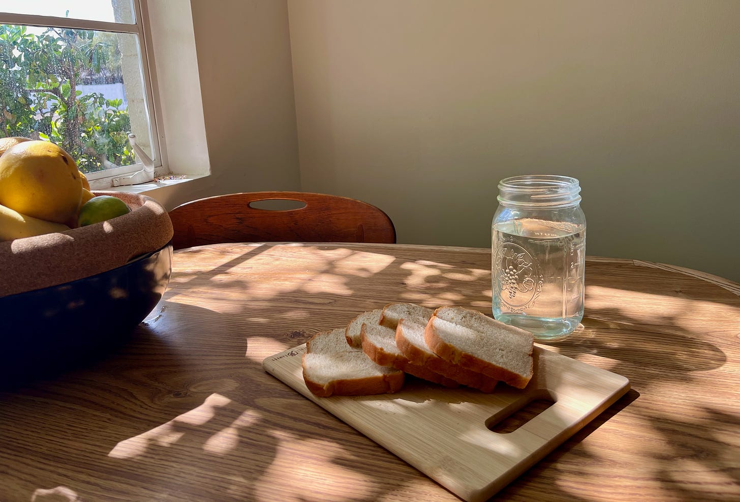 a loaf of bread, sliced on a cutting board, sitting on my kitchen table next to a mason jar of water, looking pretty in the sunlight