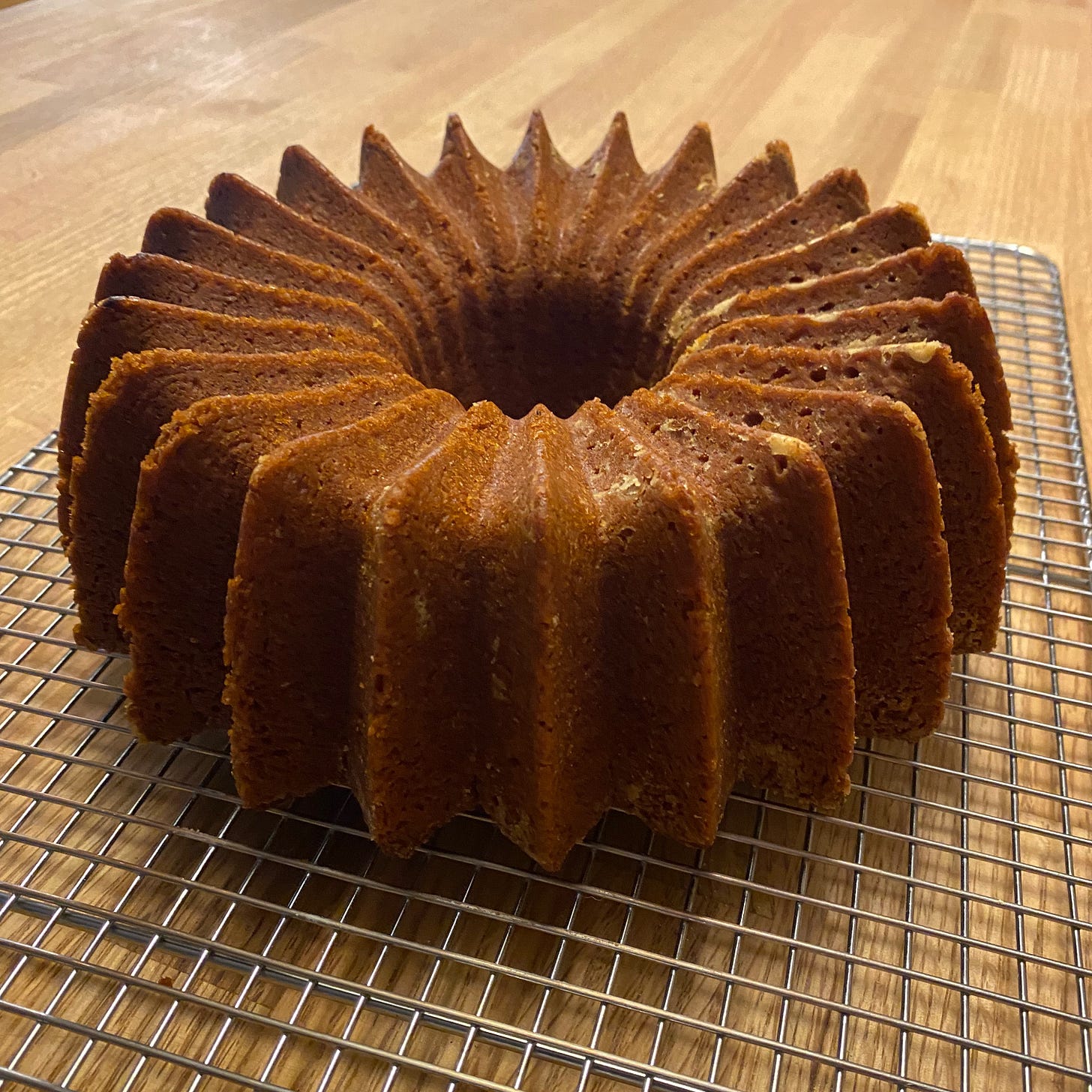 A round, golden brown bunt cake with many small ridges sits on a cooling rack on a kitchen island.