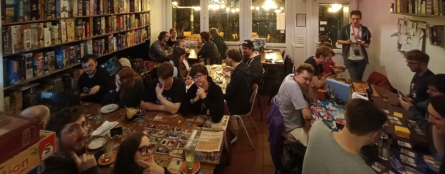 Many attendees are split across four large tables while playing board games in a board game café in Cologne