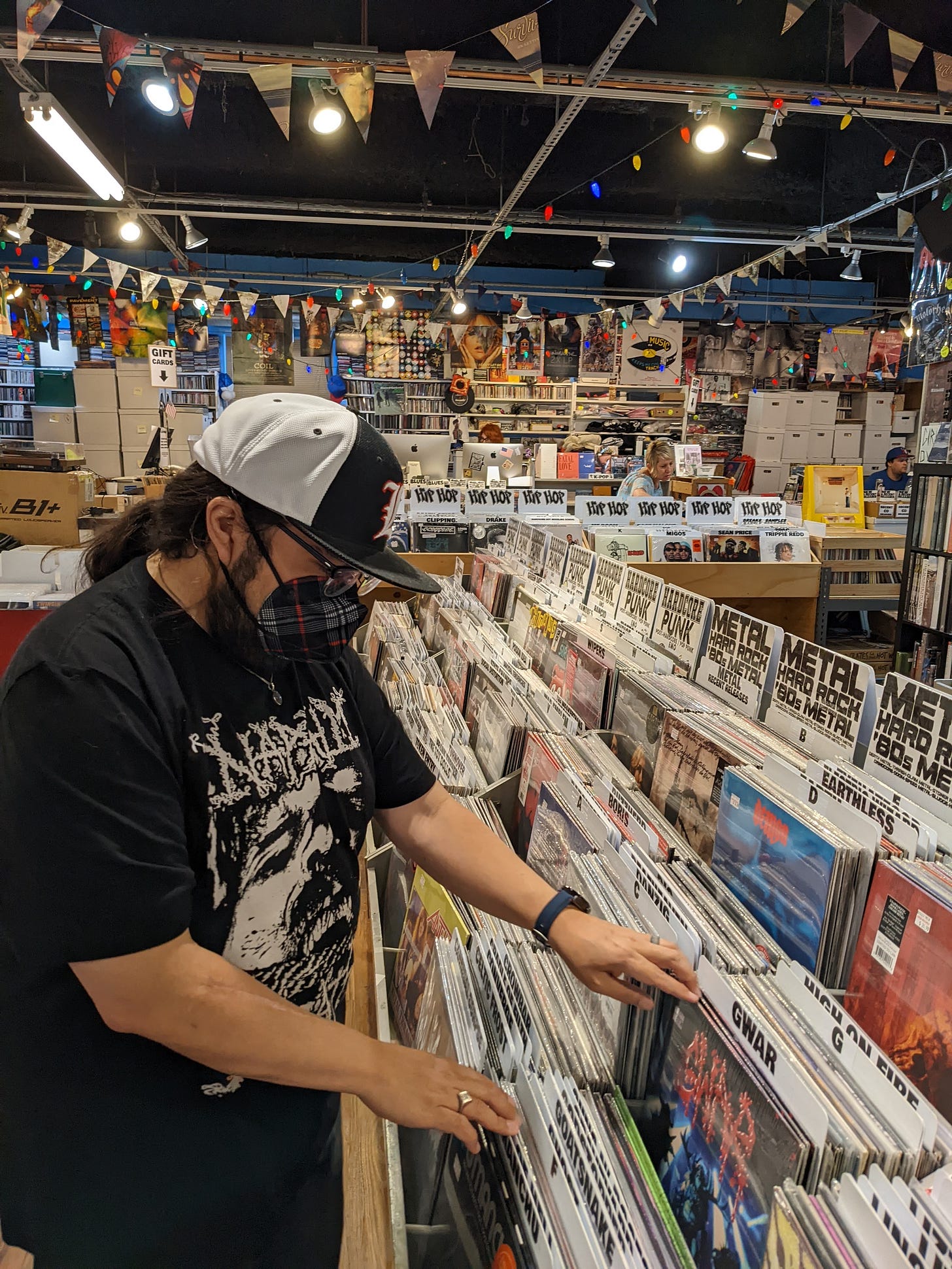Young man wearing a plaid N95 mask flips through records in sales rack at Siren Records in Doylestown PA.