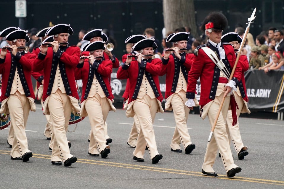 Military musicians in colonial-era uniforms march in a parade.