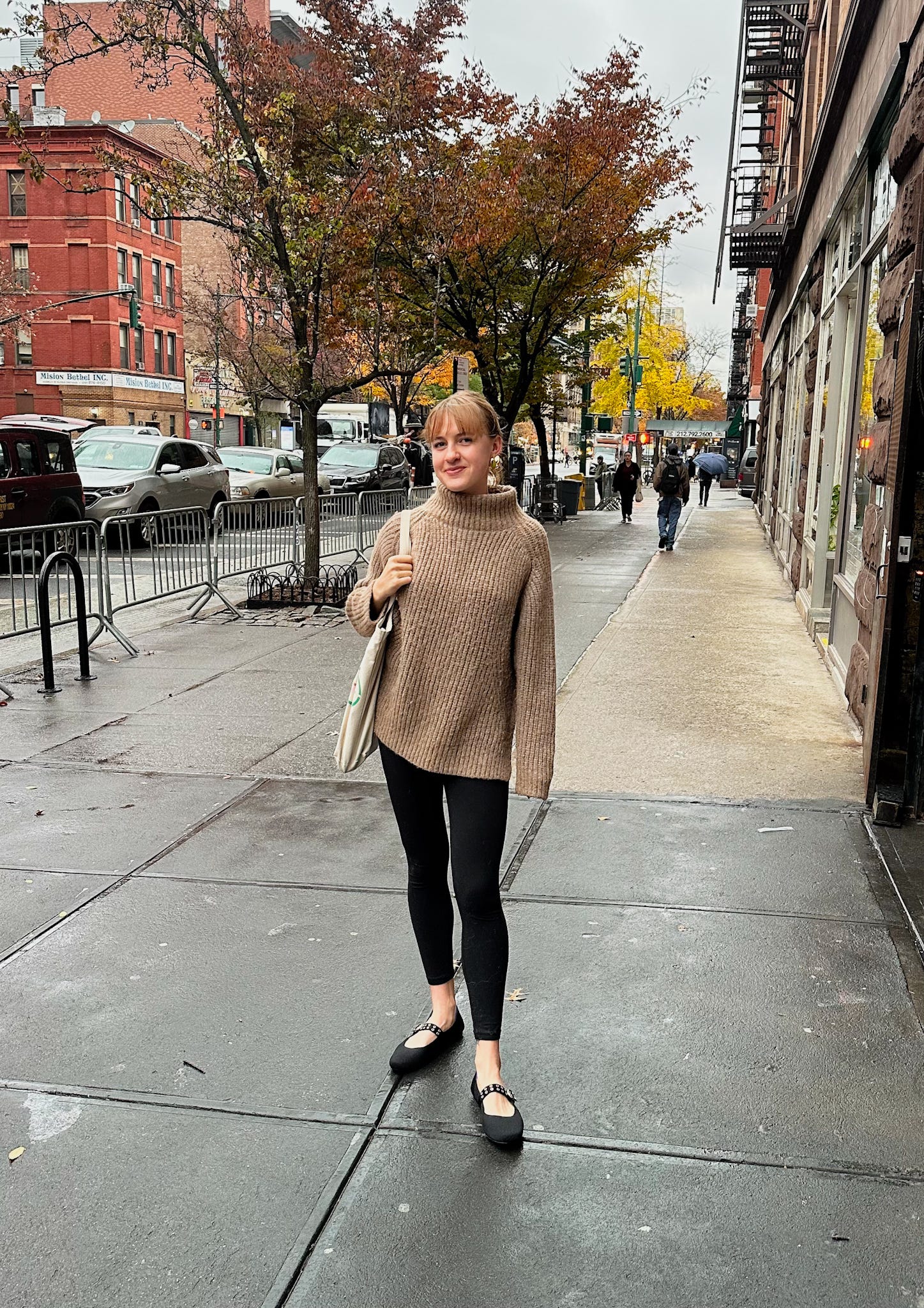 Jackie Warehime in a tan turtleneck sweater on the sidewalk in the Upper West Side, NYC.