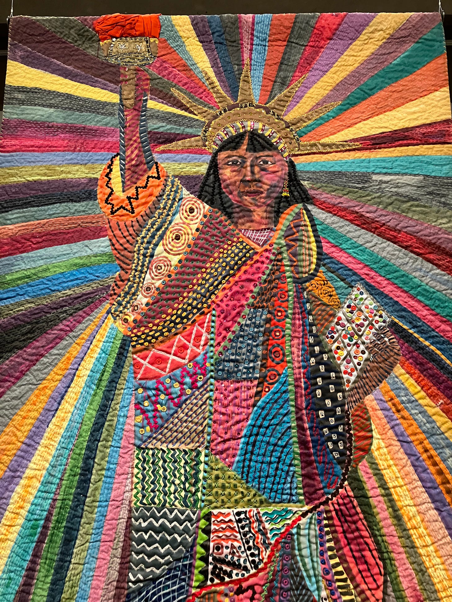 quilted panel of artist's self portrait as Statue of Liberty, with rainbow colors radiating outward