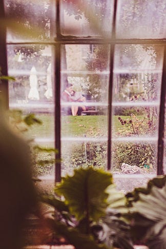 Image of window looking out into a garden with a couple sitting on a bench in the distance.