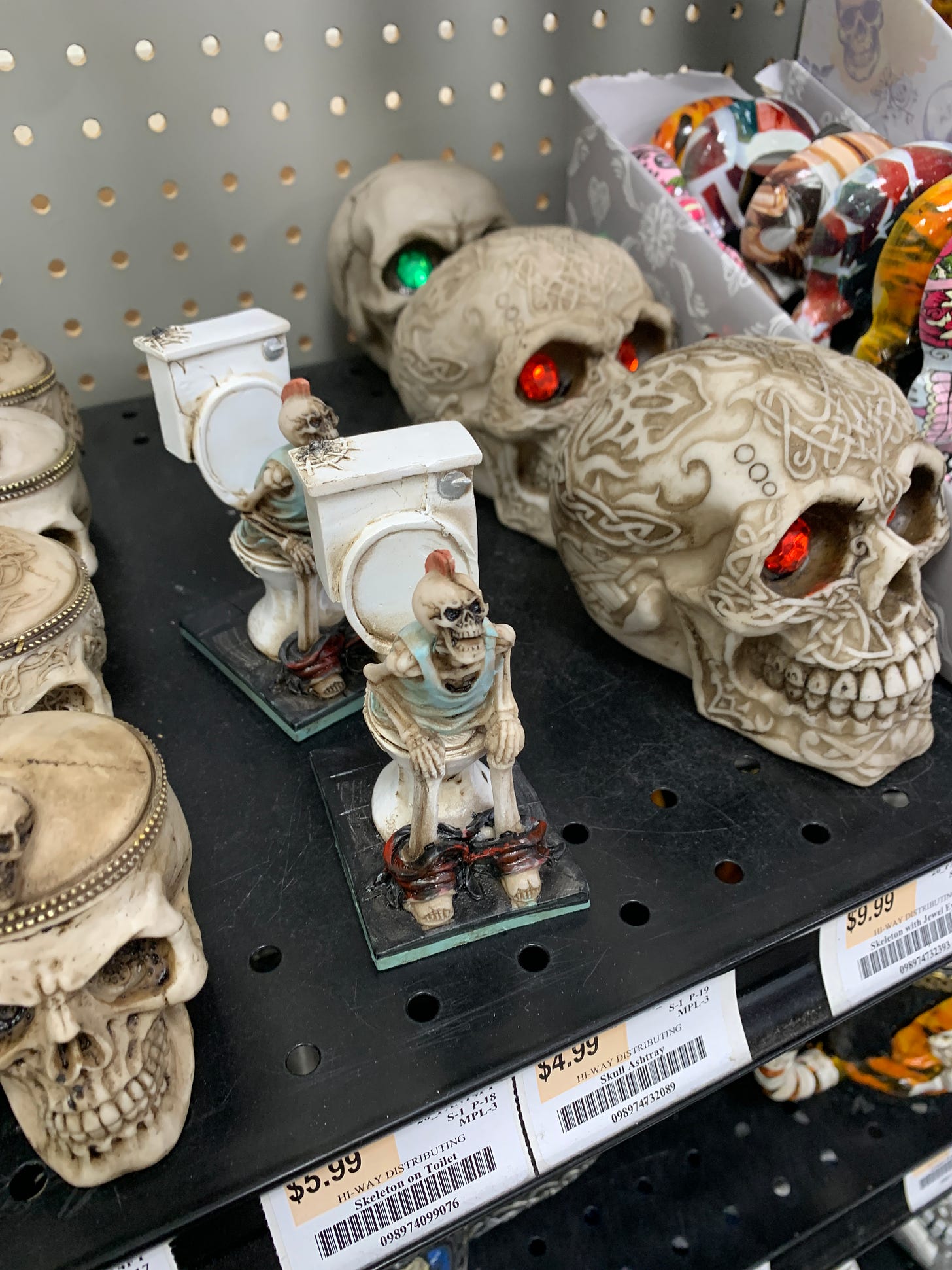 a photo of a shelf in a store. on the shelf are several plastic skeleton heads and a plastic skeleton that is screaming while sitting on the toilet