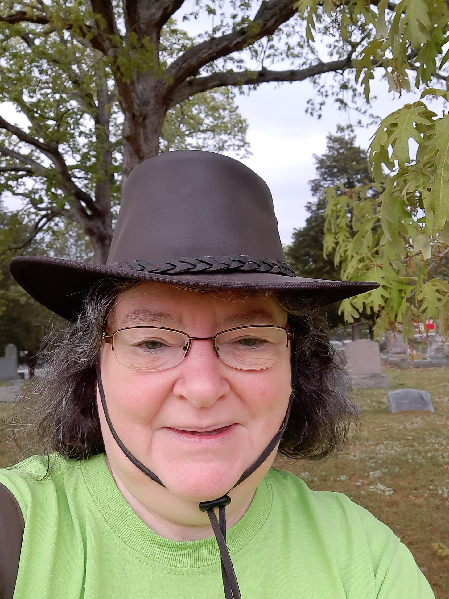 Your author: who is a white woman in a leather hat standing by an oak tree in a local cemetery.