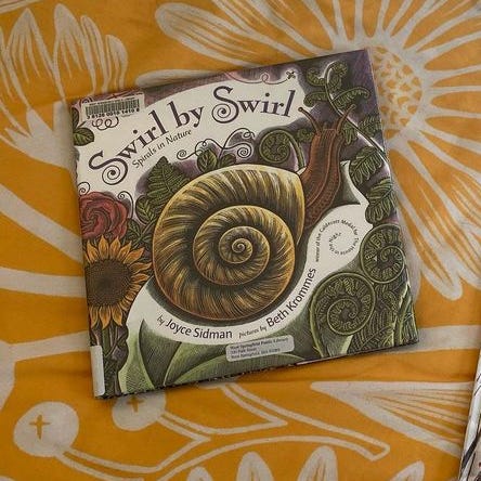 This book lies on a yellow bedspread patterned with white flowers and vines.