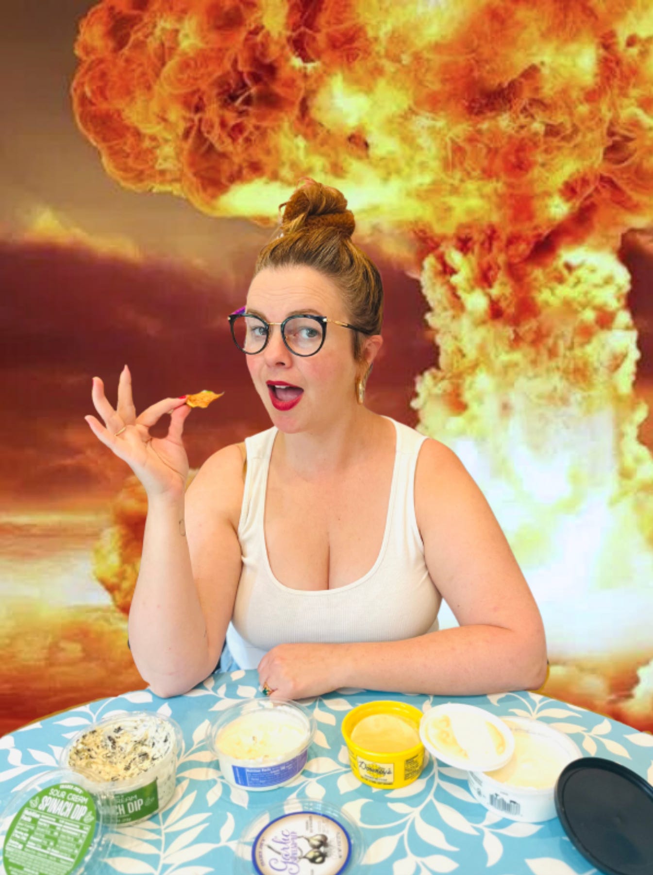 Amber sits at a table about to eat a tortilla chip. Various dips are on the table in front of her. Behind her, the background has been edited to look like a massive explosion has just gone off.