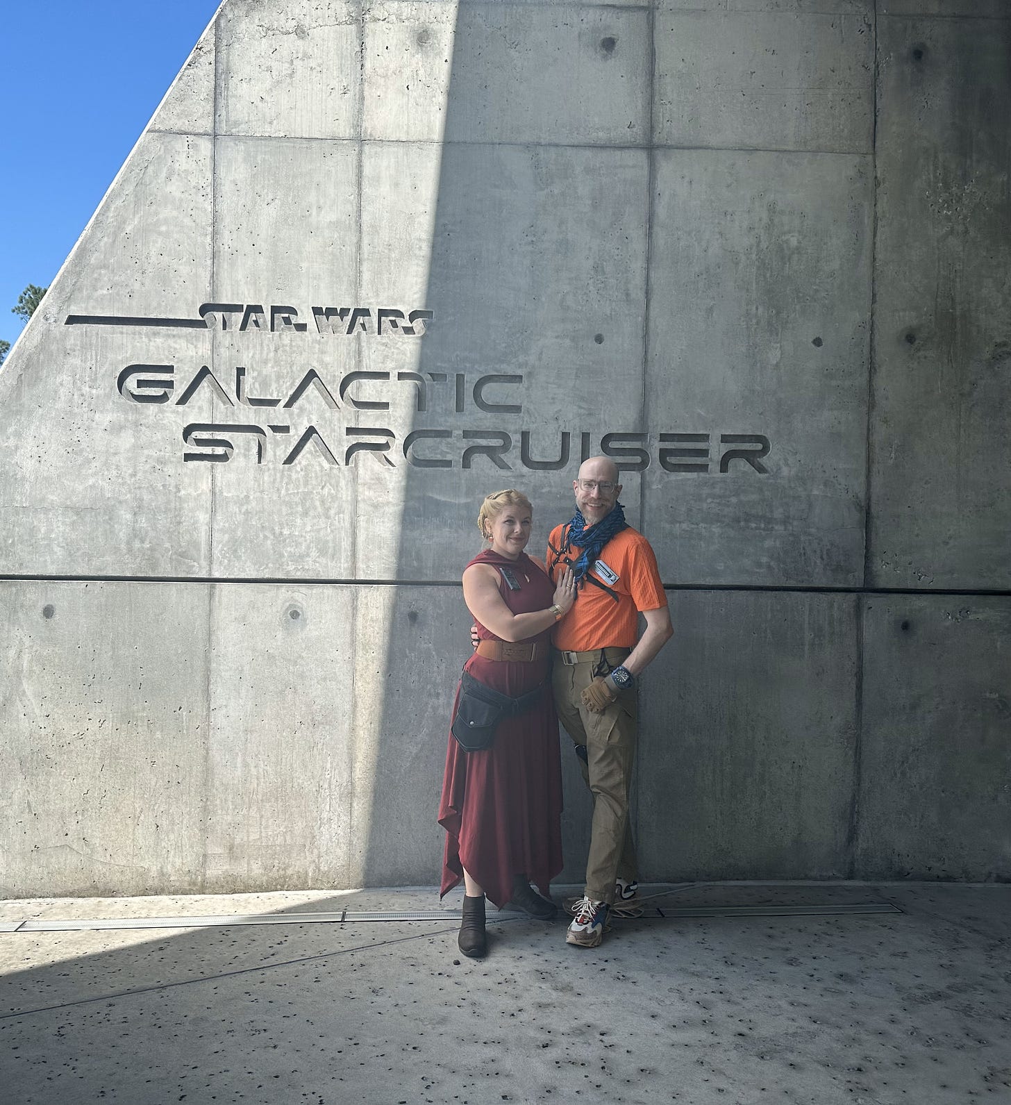 Cass and Noah, in their costumes, standing in front of the Star Wars Galactic Starcruiser concrete signage