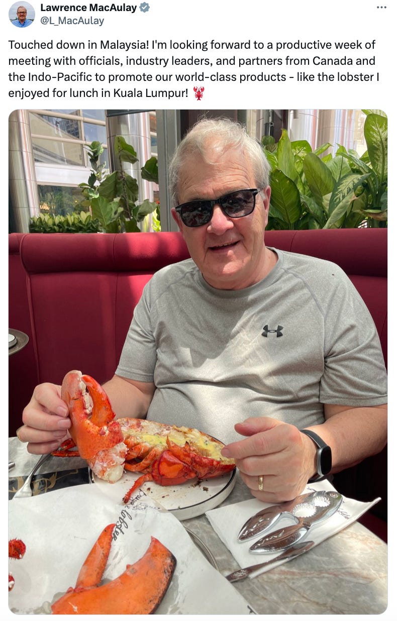 A man sits at a booth and smiles at the camera while eating a lobster.