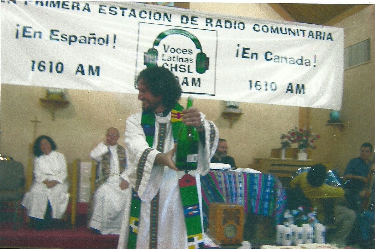 A clergyperson holds up a bottle at a christening event for AM 1610 community radio station circa 2004.