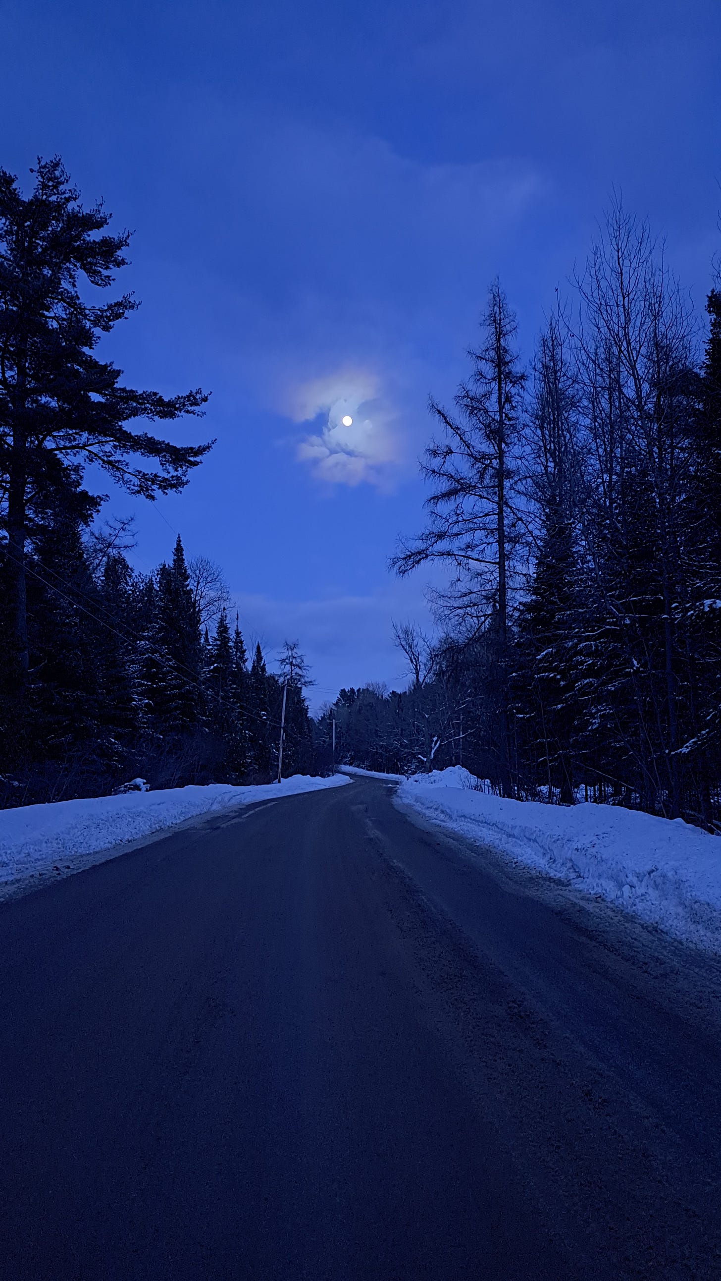 The moon is seen through some light clouds over a quiet country road in the Adirondacks