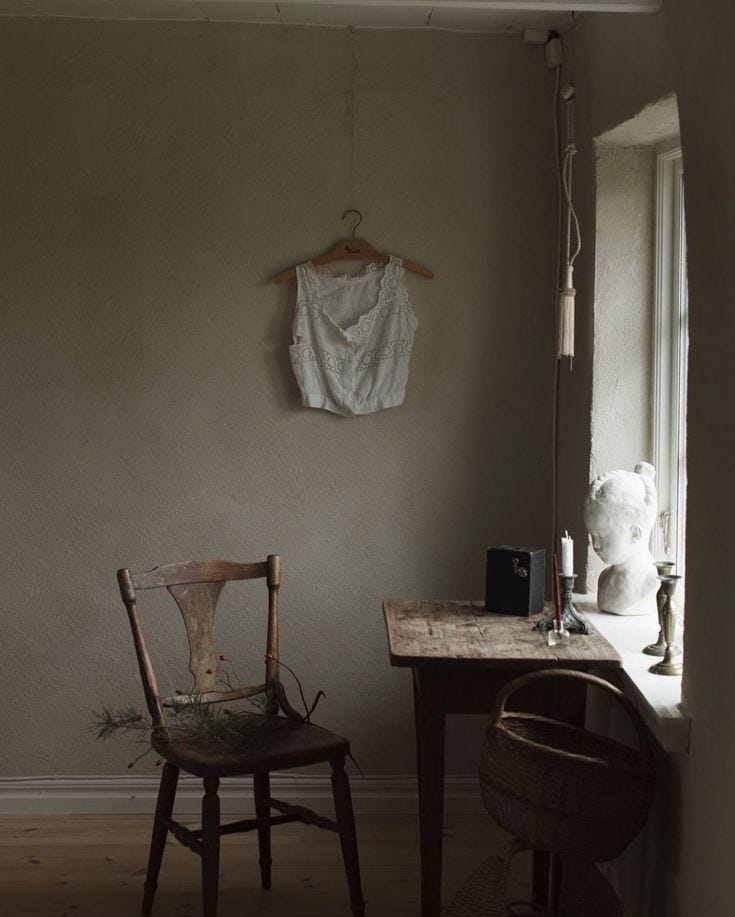 This may contain: an old chair sitting in front of a window next to a desk with a vase on it