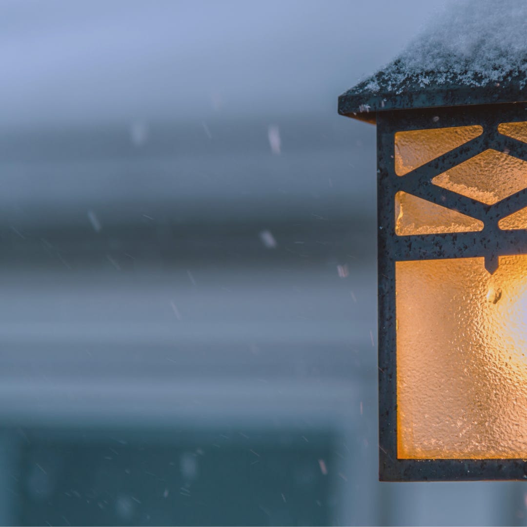 a porch light in the dark on a snowy night