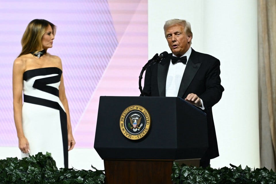 Donald Trump speaking at a podium, with Melania Trump standing behind him.