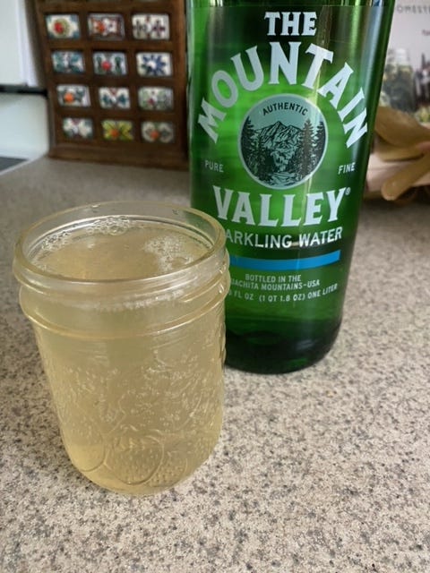 glass mason jar filled with a drink next to a green bottle of sparkling water