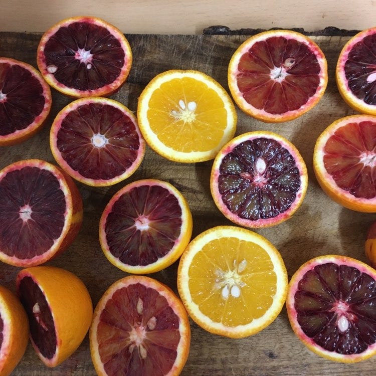 A chopping board filled with halves of oranges, mostly blood oranges and some orange ones 