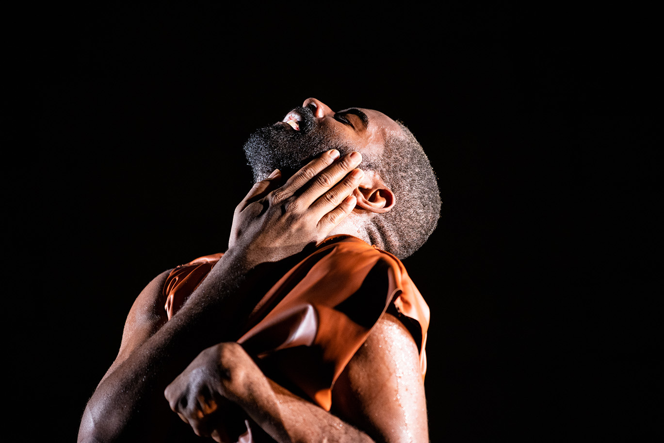 A Black Disabled man is looking up but his eyes are closed. One hand caresses his face, the other is pulled tight towards his body. Jerron Herman. Photo: Maria Baranova. Courtesy the artist and Abrons Arts Center, New York.