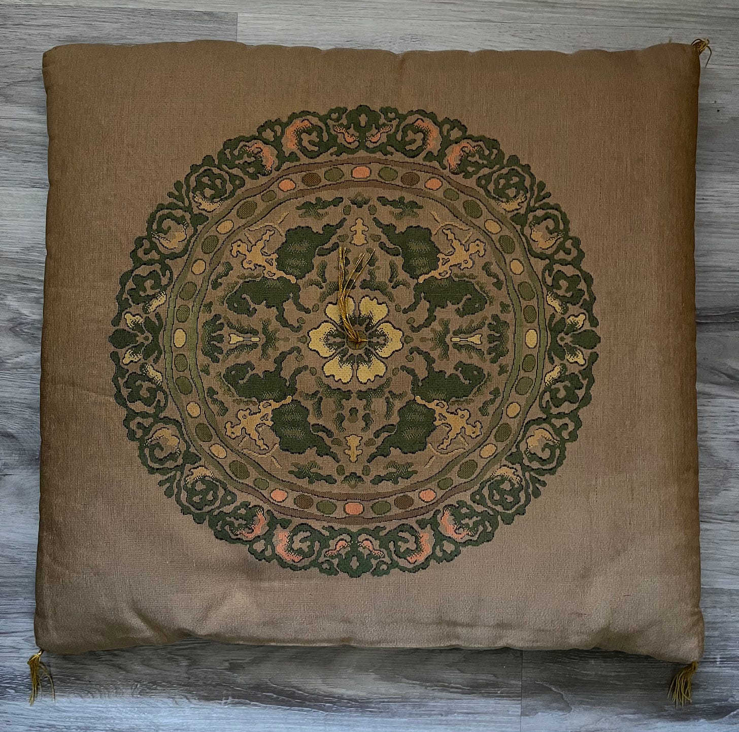A golden ochre flat square pillow with flowers, horses, and archers on it in greens, golds, and pinks.