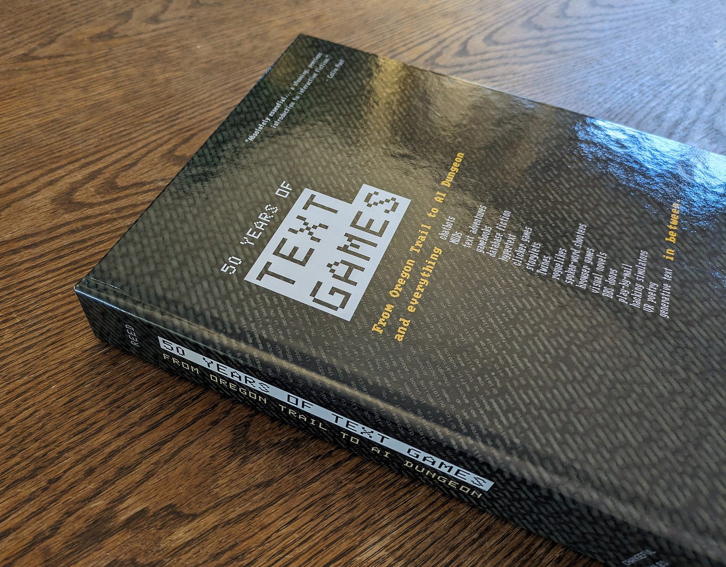 The casebound print-on-demand edition of 50 Years of Text Games, with cover design featuring blurry green terminal text behind the title.