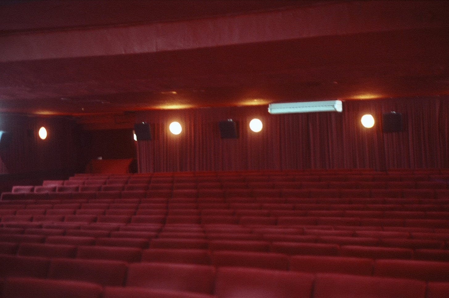 Inside the downstairs screen of the Prince Charles Cinema. Rows of red velvet chairs, red ceilings, and walls draped in red curtain with lights, speakers, and an air conditioning unit. Inside the downstairs screen of the Prince Charles Cinema. Rows of red velvet chairs, red ceilings, and walls draped in red curtain with lights, speakers, and an air conditioning unit.