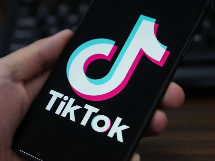 Logotipo do aplicativo TikTok mostrado no telefone de alguém sendo segurado na frente de um teclado.