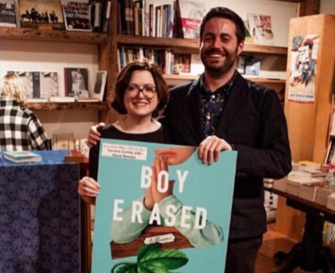 Image shows the writers Maud Newton and Garrard Conley standing behind a poster for Conley's memoir BOY ERASED