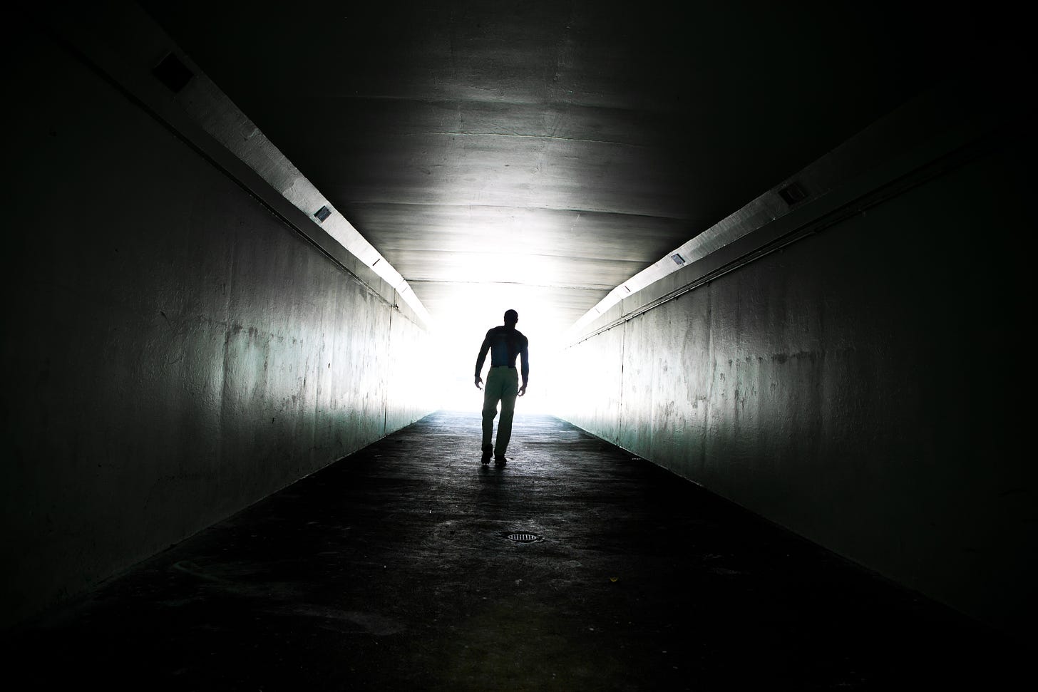 A Black and white image of the receding figure of a man in a darkened tunnel.