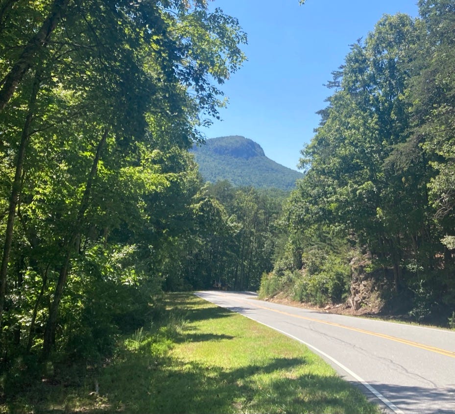 two-lane road through the trees, the peak of Hanging Rock in the distance