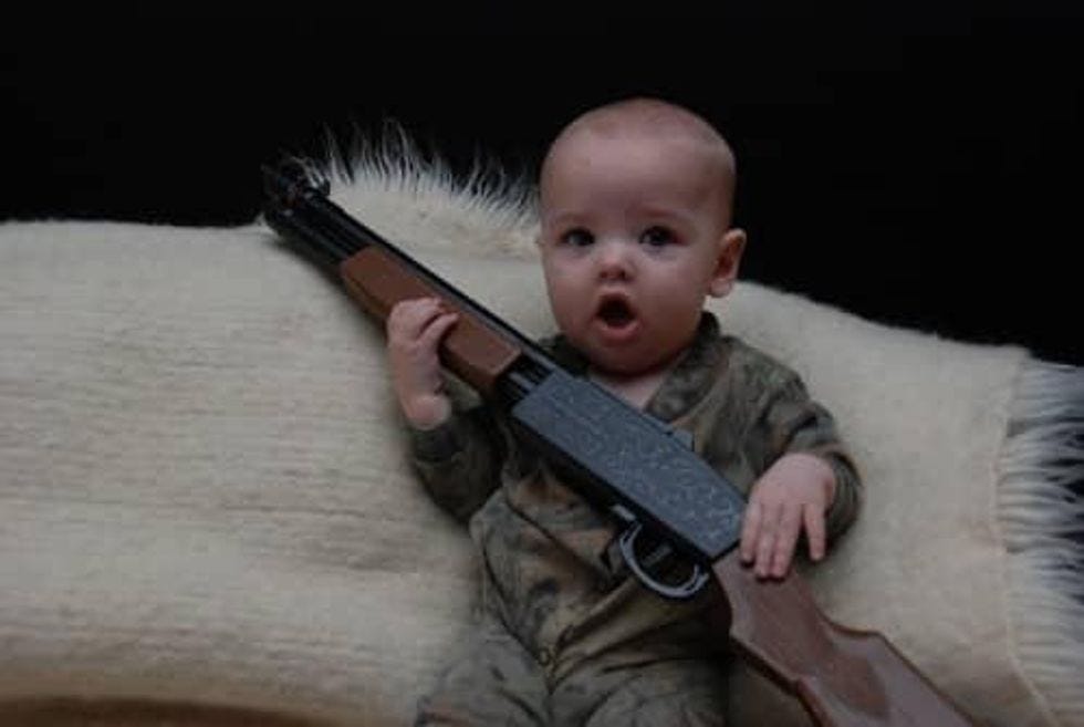 Baby in camo onesie holding a gun
