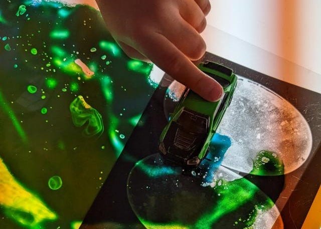 child's hand pushing a toy car over a sensory mat filled with green liquid