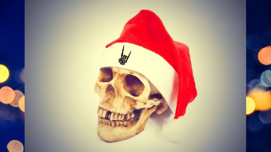 A skull wearing a santa hat grins about the devil-horns skeleton hand embroidered on his hat while lights twinkle merrily in the background