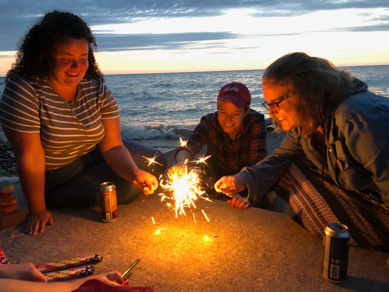 Three people lighting their sparklers, in front of the sunset